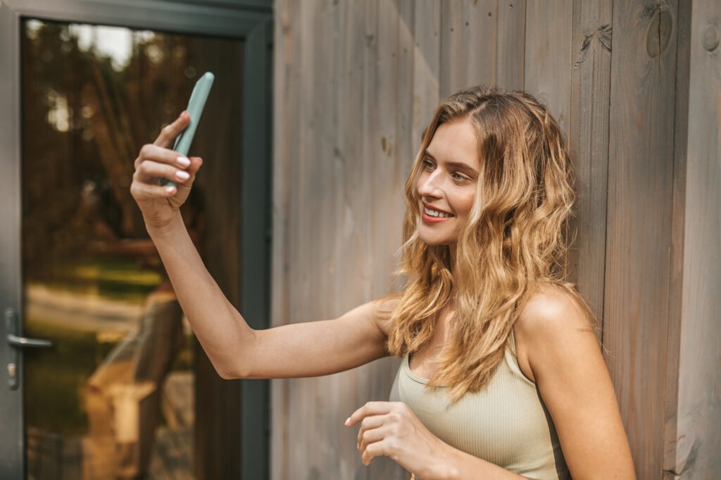 OnlyFans Social Media Marketing: Schöne Frau macht lächelnd Selfie mit Smartphone