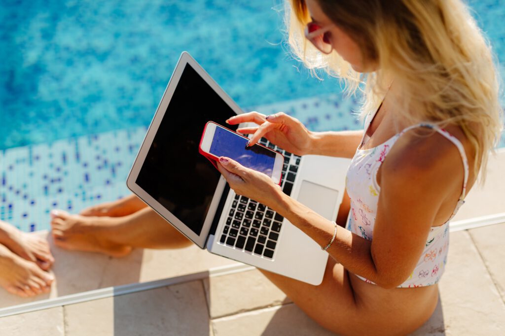 OnlyFans Creator Lifestyle & Erfolg: Frau nutzt Laptop und Smartphone am Strandpool