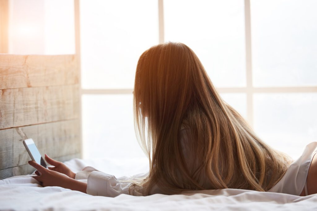 Frau liegt auf Bett und benutzt Smartphone