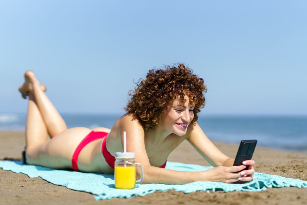 Positive OnlyFans Fan-Kommunikation: Lachende Frau an Küste mit Smartphone